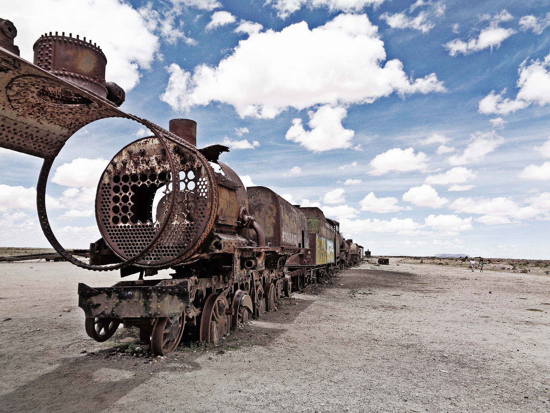 A line of abandoned train cars against a blue sky with clouds in the desert.