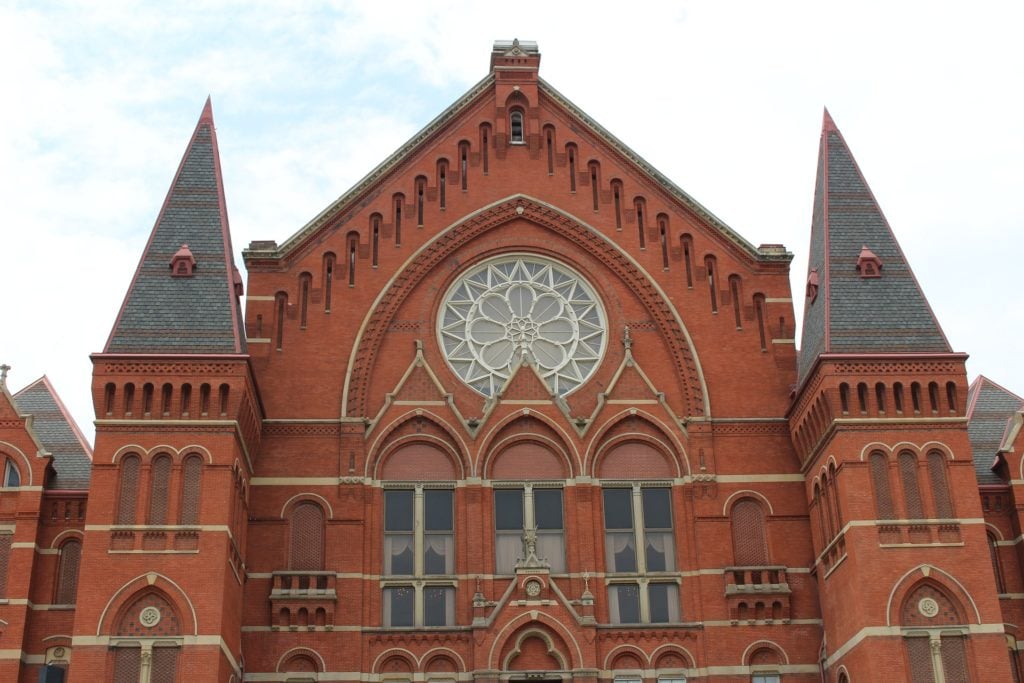 The exterior of Cincinnati Music Hall, a High Victorian Gothic building made of red brick with peaked gables and a beautiful rose window.