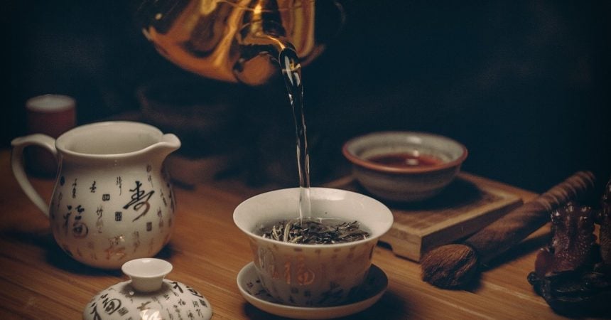 Water pouring from a silver kettle into a teacup full of loose leaf tea