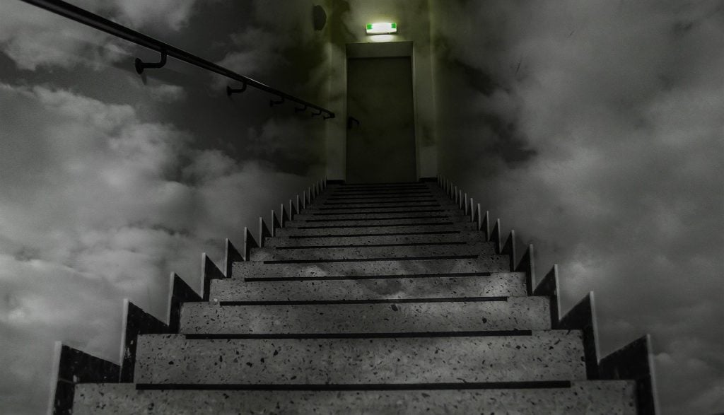 Looking up a flight of dark, spooky stairs to a closed door at the top