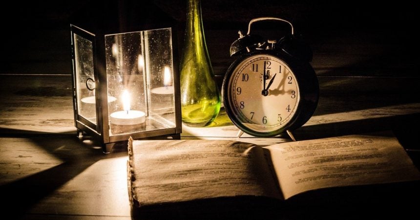 A desk with an old book, a lantern, and an old-fashioned alarm clock on it