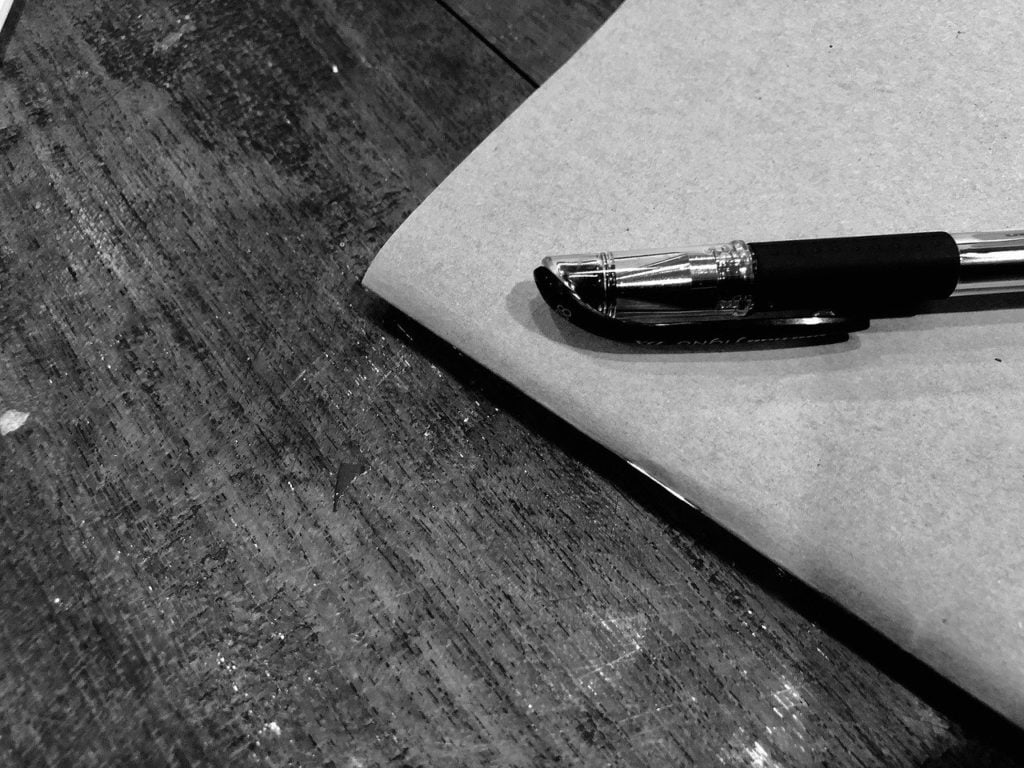 A pen and a notebook sitting on a wooden surface