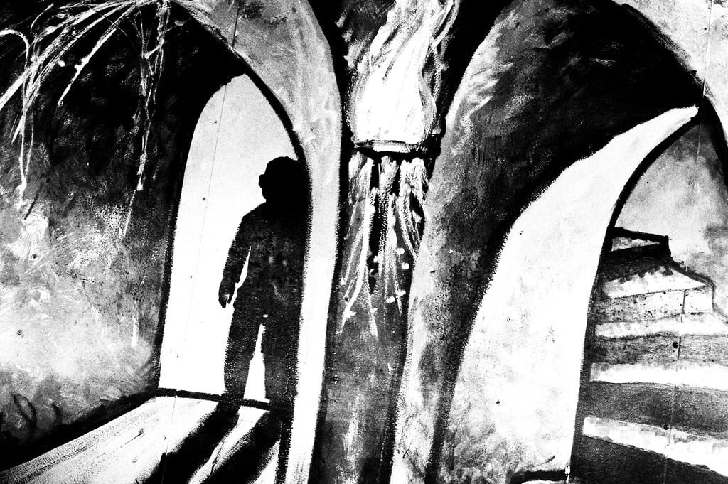 A black and white illustration of a shadowy, humanoid figure in a dark room