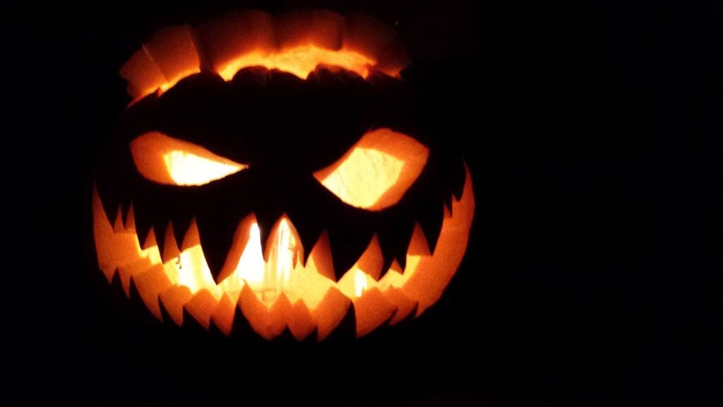 A jack o' lantern with sharp teeth, lit, in the dark