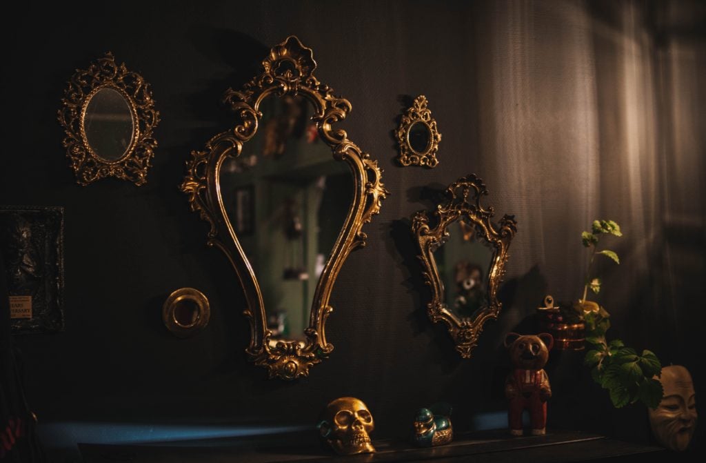 Many ornate, gold-framed mirrors arranged on a dark wall
