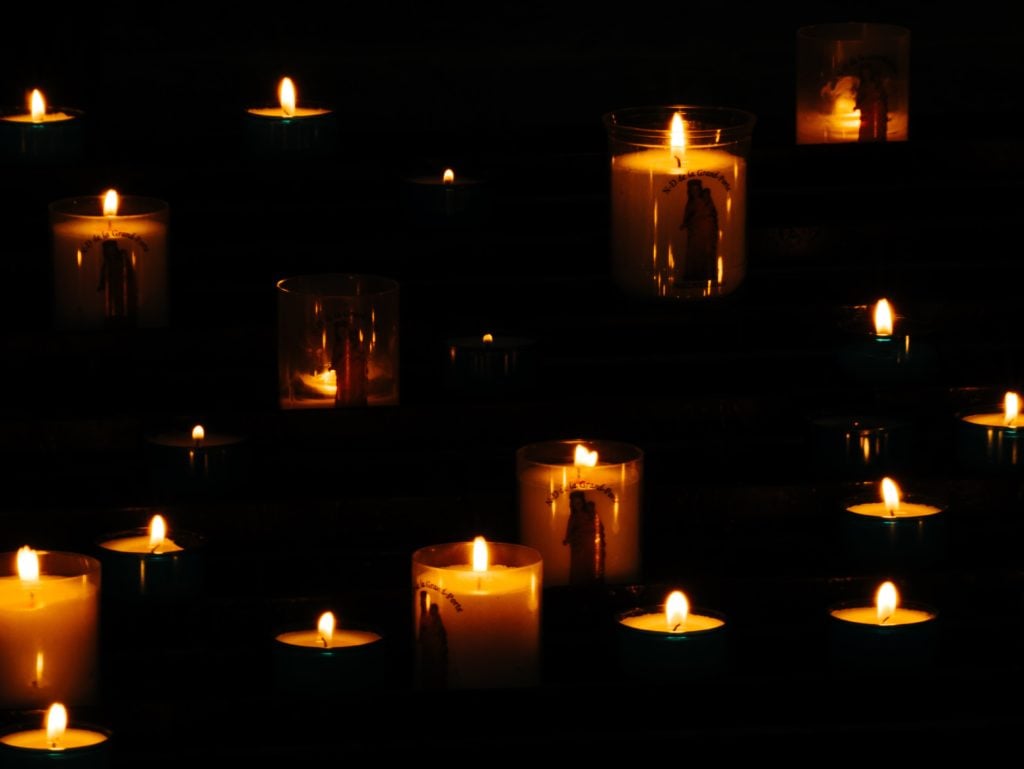 A large quantity of lit candles glowing in the darkness