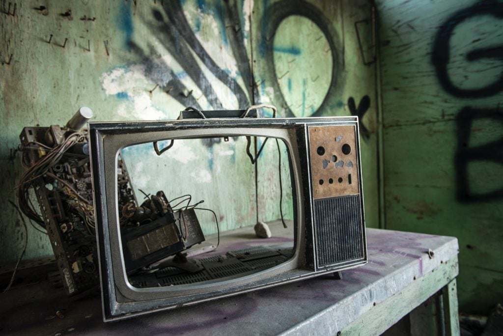 An abandoned, vintage television with a busted-out screen