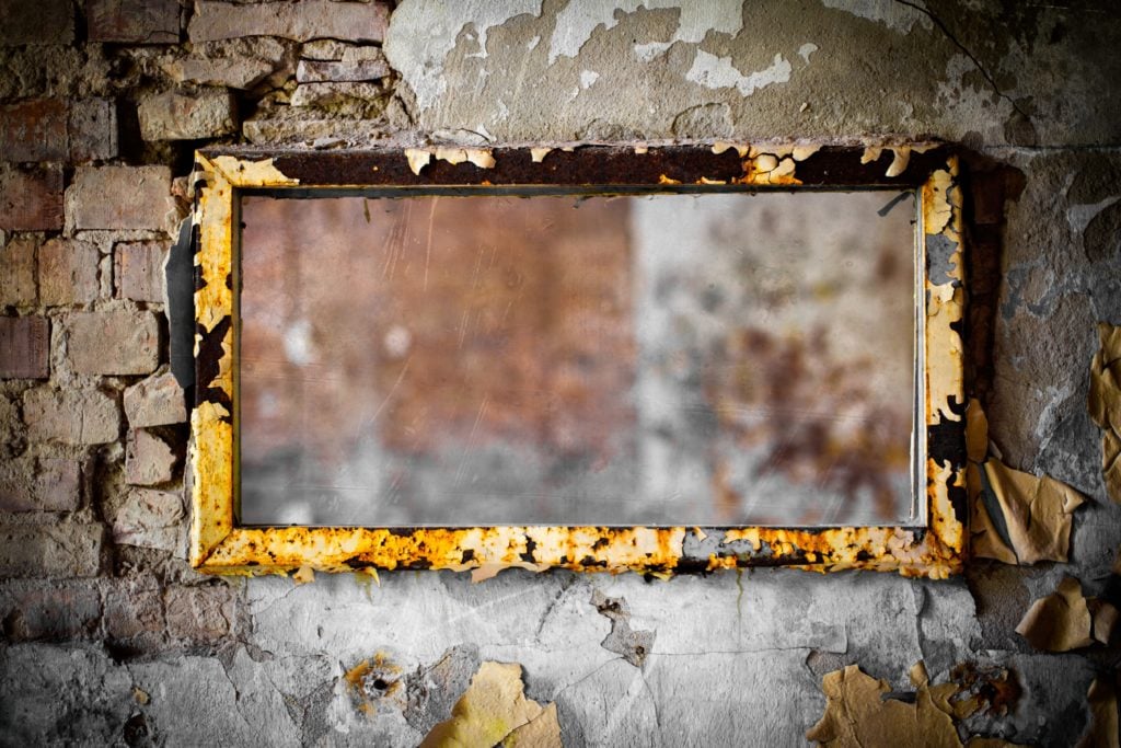 A mirror with a flaking frame hanging on a decaying wall