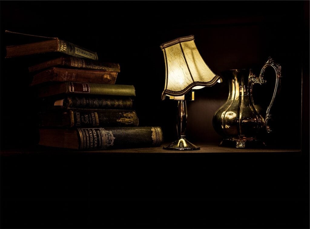 a desk with a stack of books and an old fashioned lamp
