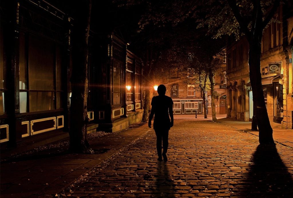 The silhouette of a woman walking down a street in a city at night