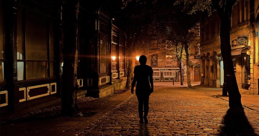 The silhouette of a woman walking down a street in a city at night