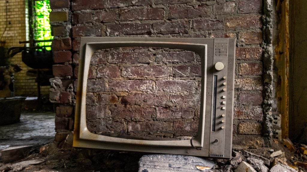 An abandoned TV with a brick wall visible through its screen
