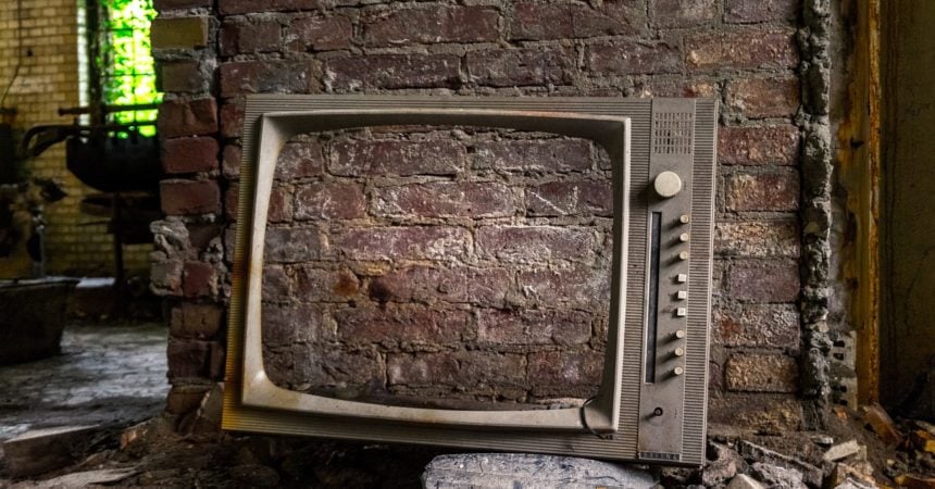 An abandoned TV with a brick wall visible through its screen