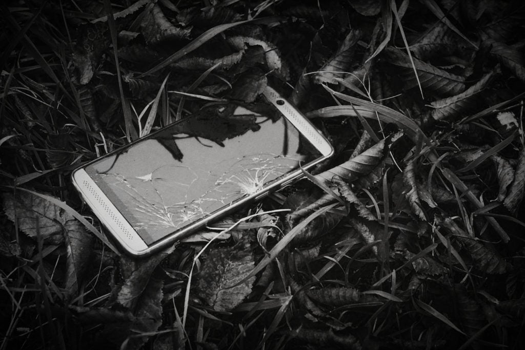 A smartphone with a broken screen lying in a pile of leaves