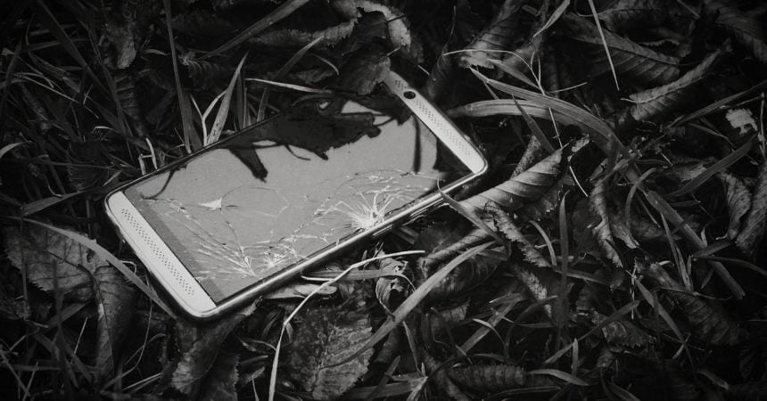 A smartphone with a broken screen lying in a pile of leaves