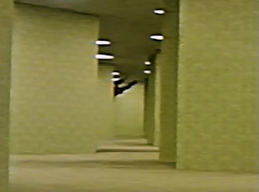 Black tendrils creeping around the corner of a yellow hallway in the Backrooms, from the video Backrooms - Motion Detected