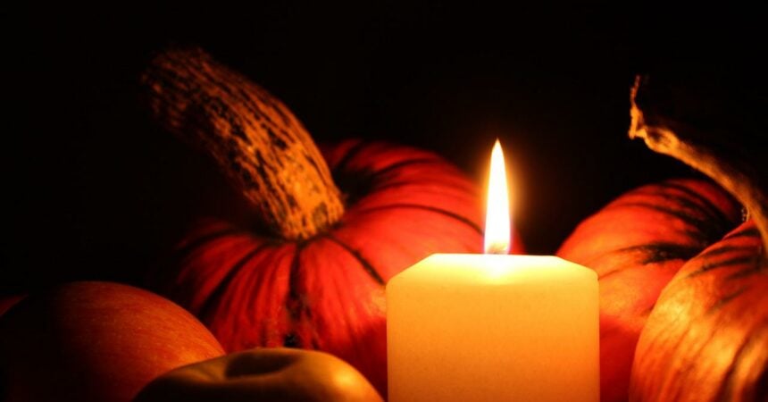 A pile of pumpkins in the dark surrounding one lit candle