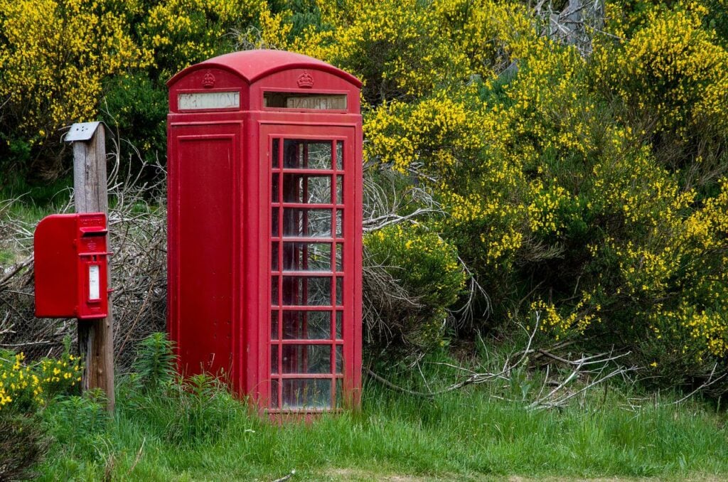A red British phone booth in a slightly overgrown area by the side of the road