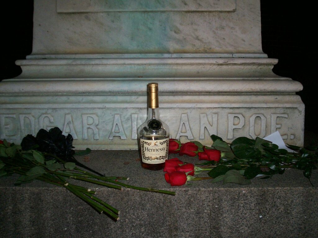 A photograph of the Edgar Allan Poe memorial in Baltimore, with a bottle of cognac and several black and red roses laid before it