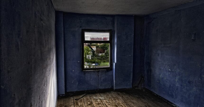An empty room in an abandoned home with a wood floor, blue walls, and one window