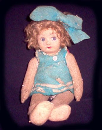 A heat-pressed felt doll wearing a blue dress with a blue hair bow. She is called Pupa, and she is an allegedly haunted doll