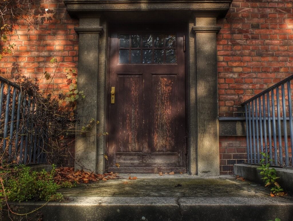 The impressive wooden front door of a large brick house covered in vines