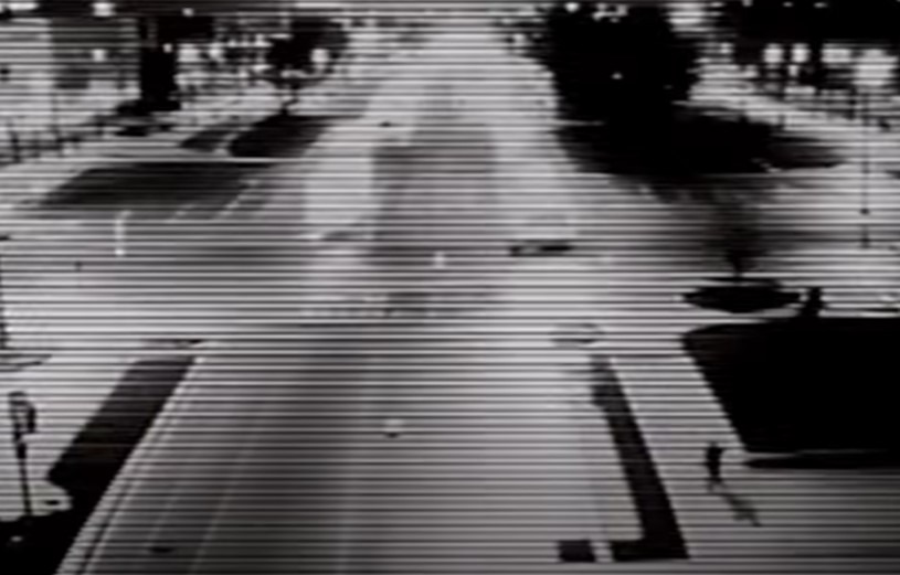 Black and white security footage of a street with a person in the lower right hand corner