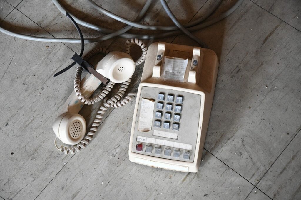 a white push button telephone, dusty and sitting on the floor