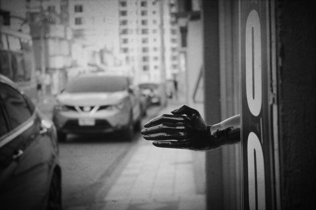 a black mannequin hand reaching out from an alley onto a busy city street