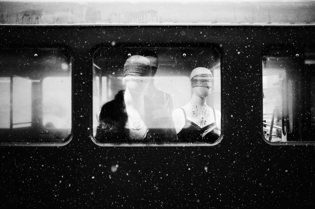 two retail mannequins standing on a train, viewed through the window