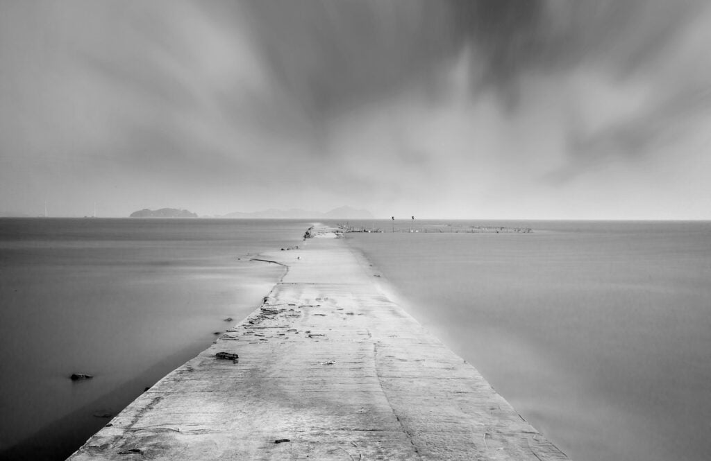 a black and white photograph of an empty, cement path in an empty wasteland 