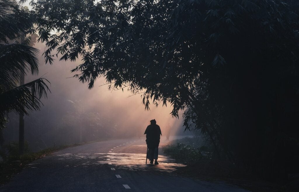 a person, silhouetted, walking down a forested road in the fog