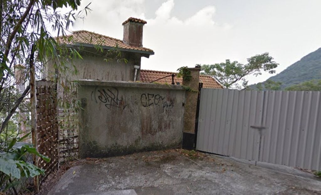 the exterior of Dragon Lodge in 2013, viewed from Lugard Road. There are fences with lots of graffiti, with the roof of a derelict house visible behind