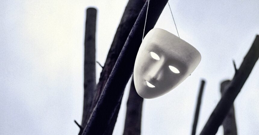 a blank, white, full face mask hanging from a large, bare tree branch