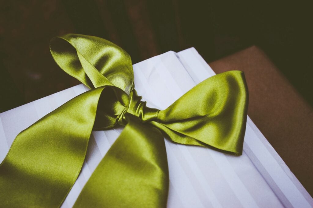 a green ribbon tied into a fancy bow lies on a white square of cloth
