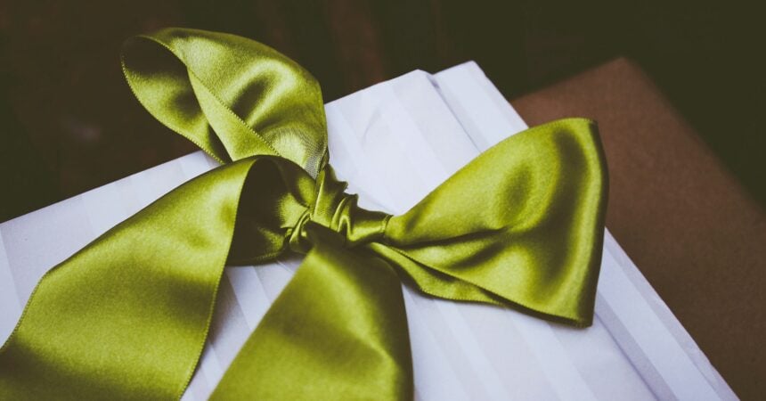 a green ribbon tied into a fancy bow lies on a white square of cloth