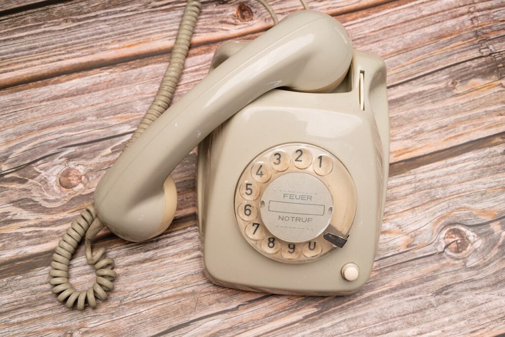 a white, vintage rotary telephone on a light wood surface