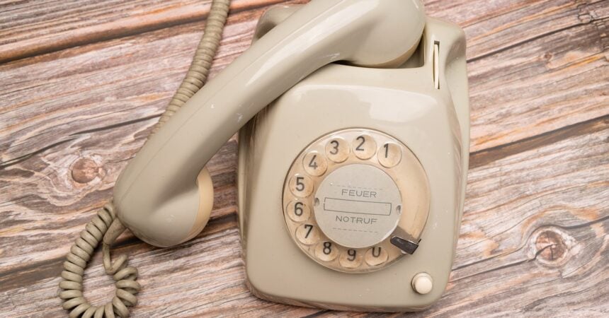 a white, vintage rotary telephone on a light wood surface