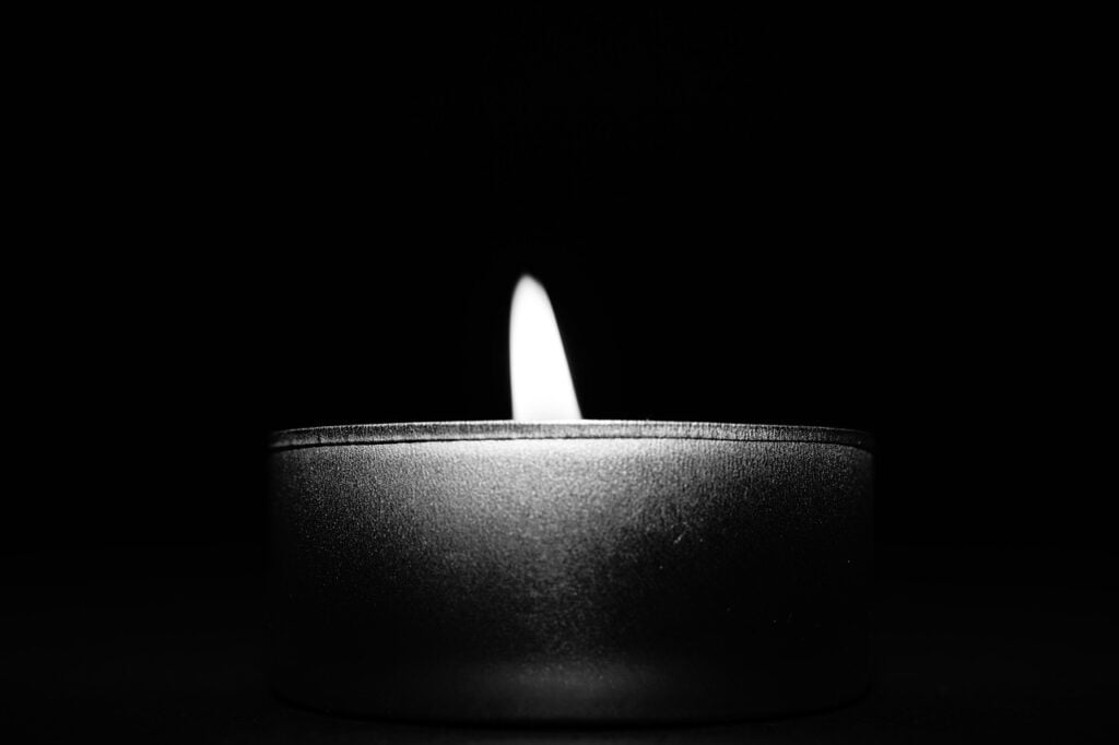a black and white photo of a lit candle in the dark