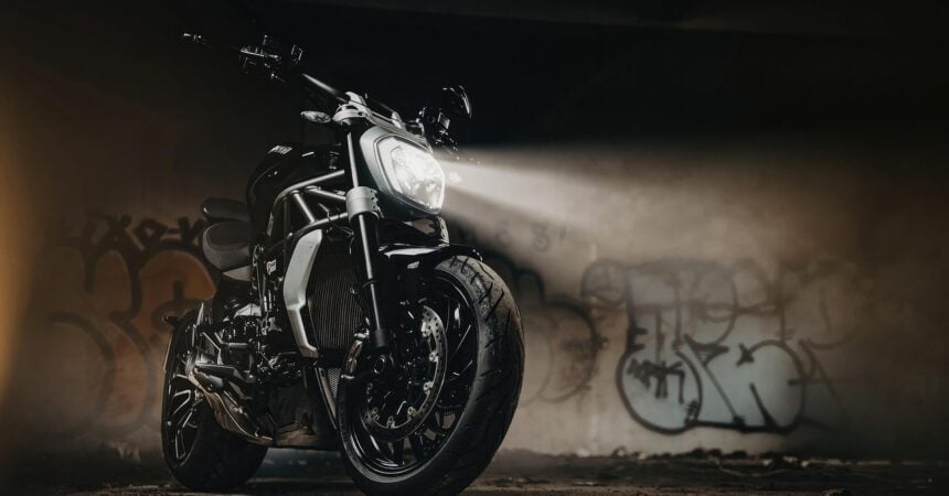 a motorcycle parked with its lights on. a wall with graffiti is in the background