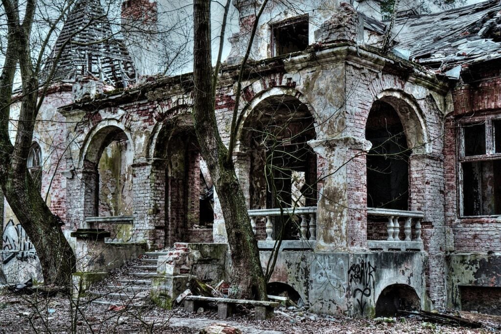the front porch of an abandoned house, with ornate arches and stone steps. a large tree blocks part of the entrance