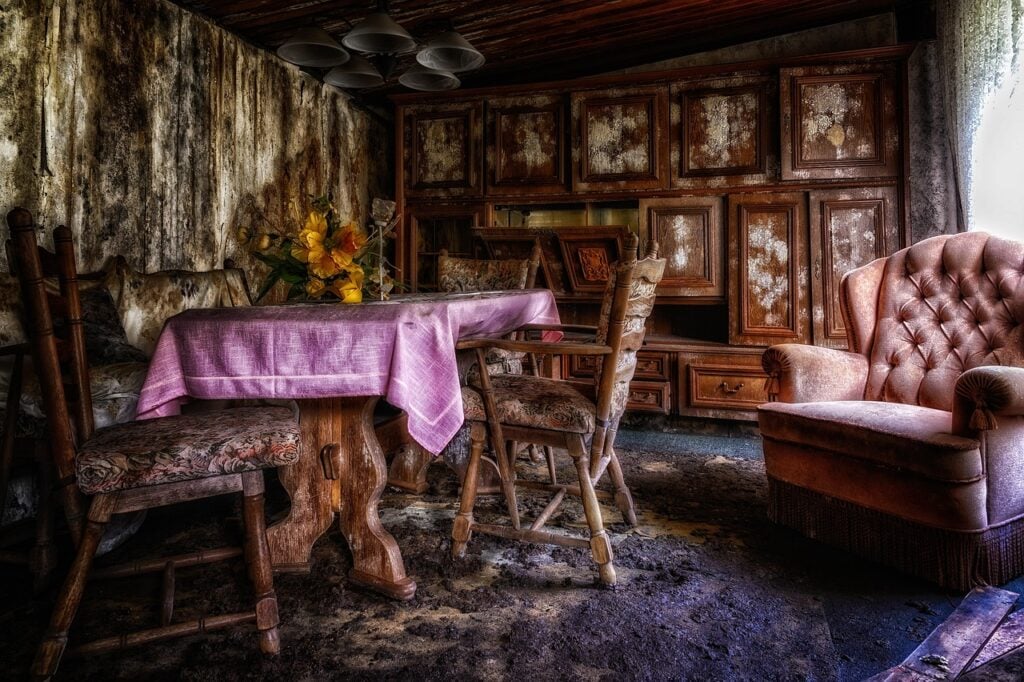 an abandoned room with a table, red tablecloth, and severaklchairs