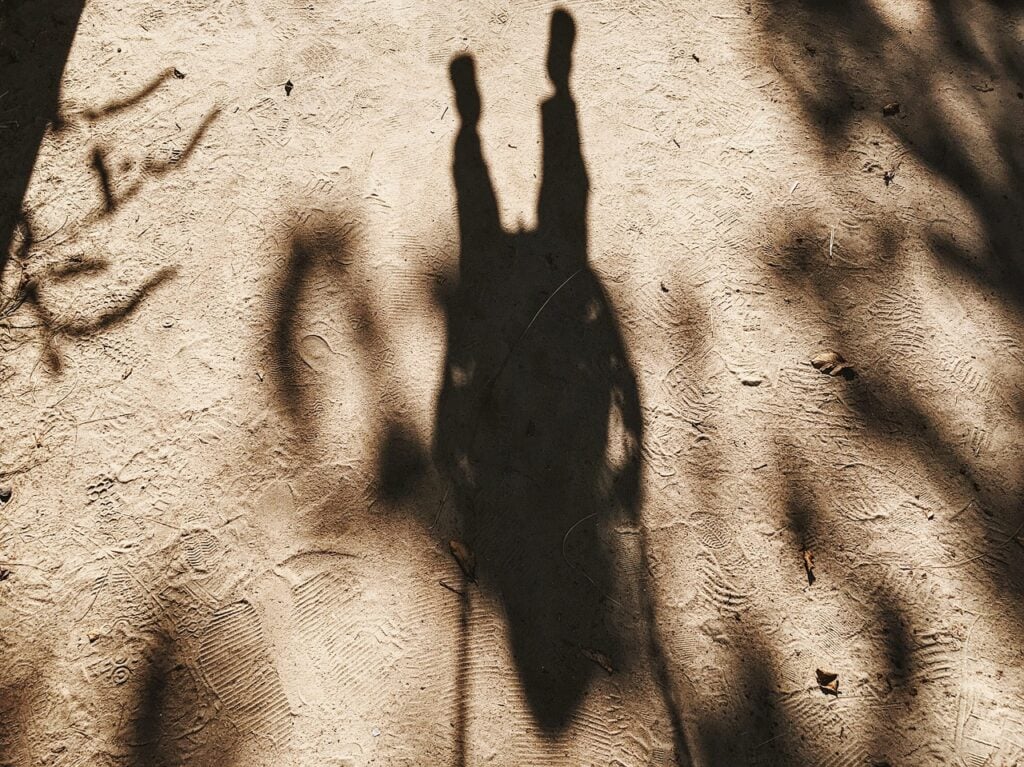 an upside-down shadow of a person on a swing seen in the sand