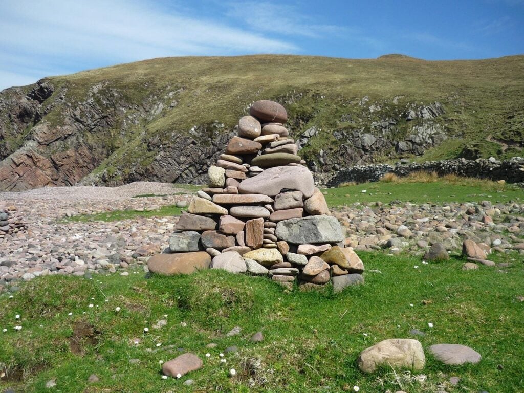 a stone cairn on a green field with hills and a blue sky in the background
