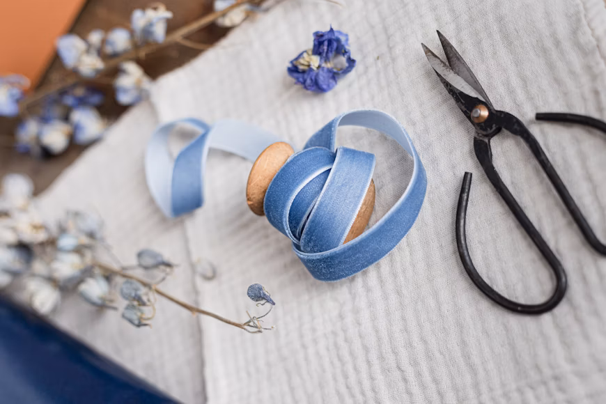 blue ribbon on white cloth with scissors and dried flowers nearby