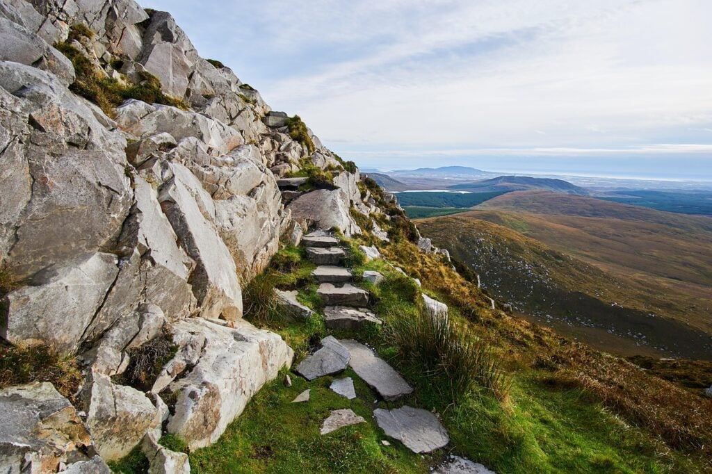 a rock path leading up a mountain with a blue sky in the background, green grass around