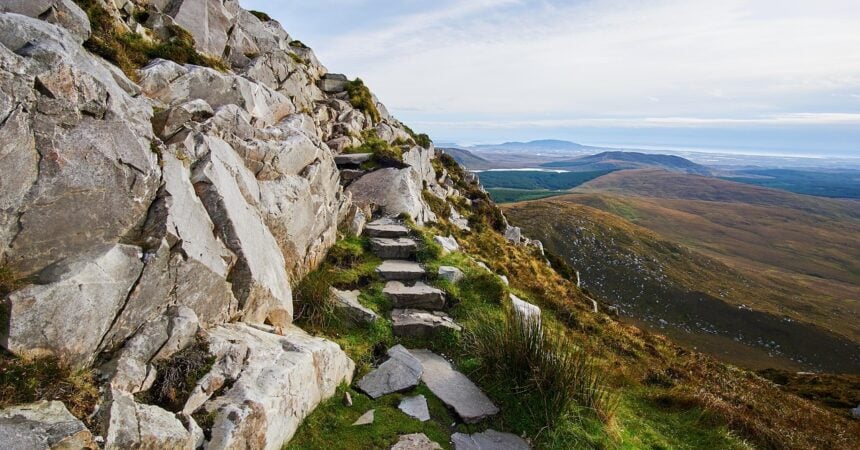a rock path leading up a mountain with a blue sky in the background, green grass around