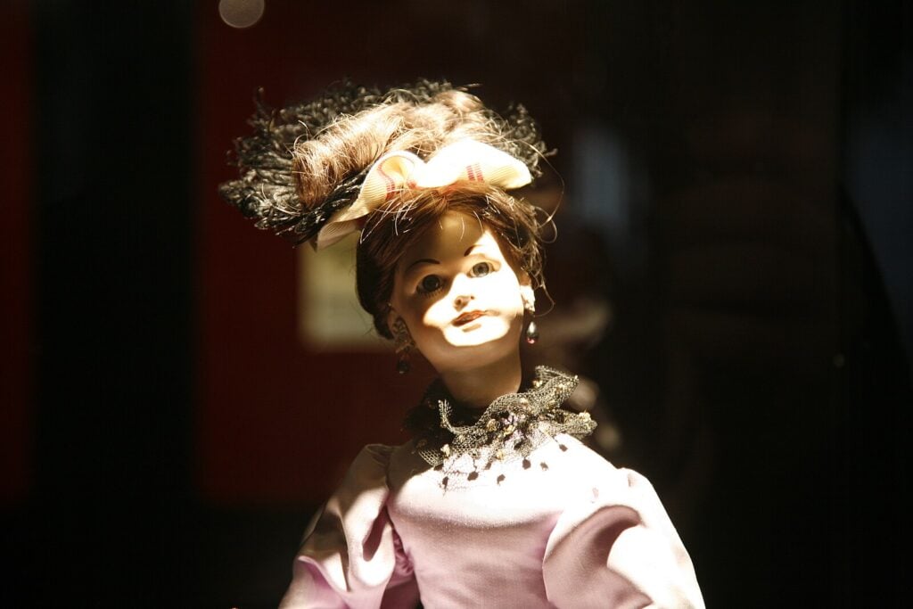 a female-presenting automaton wearing a fancy hat and dress. the uncanny valley is strong here.