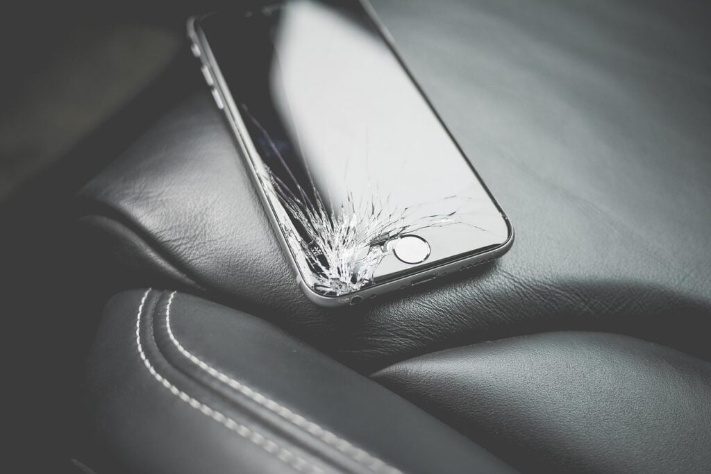 a smartphone with a smashed screen sitting on the seat of a leather-upholstered chair