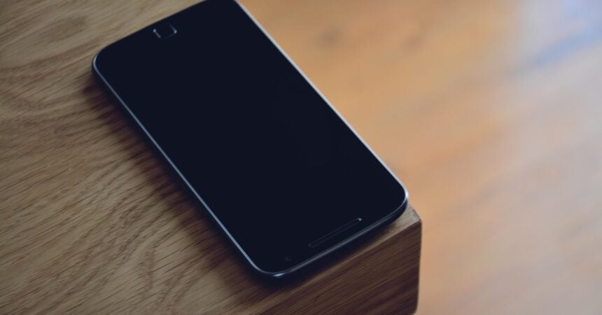 a smartphone, screen off, placed face up on a wooden surface
